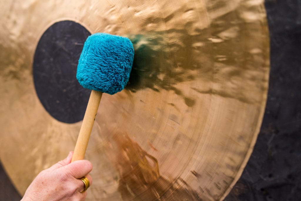 Hand hält einen Schlägel und schlägt einen Gong